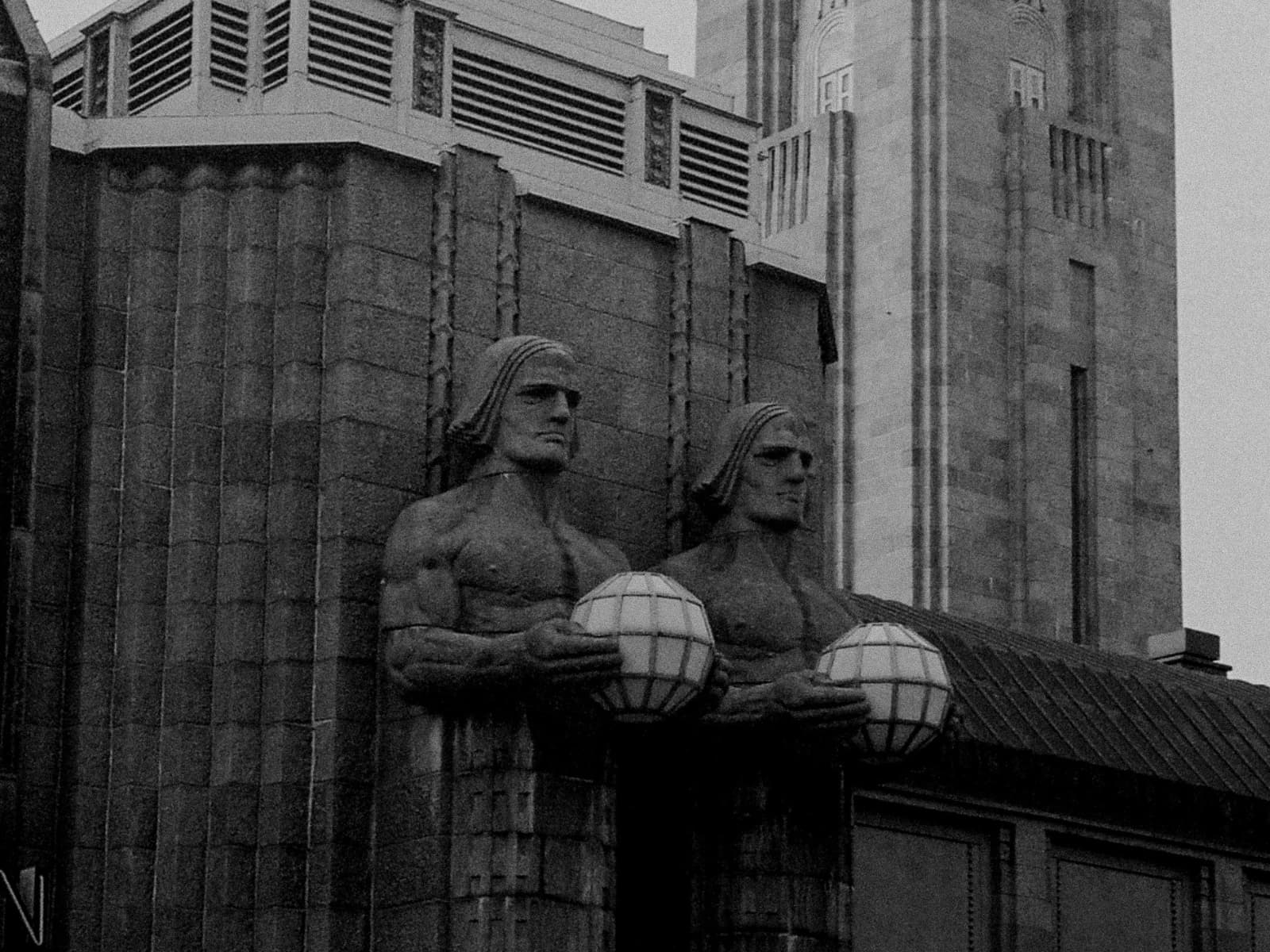 Two sculpted figures holding globe lamps above an architectural entrance
